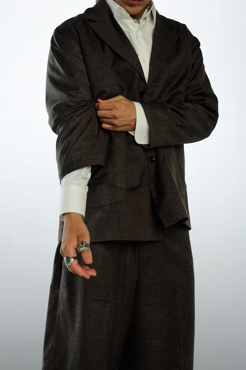 Brown suiting worn open over a white shirt, with wide pleated trousers